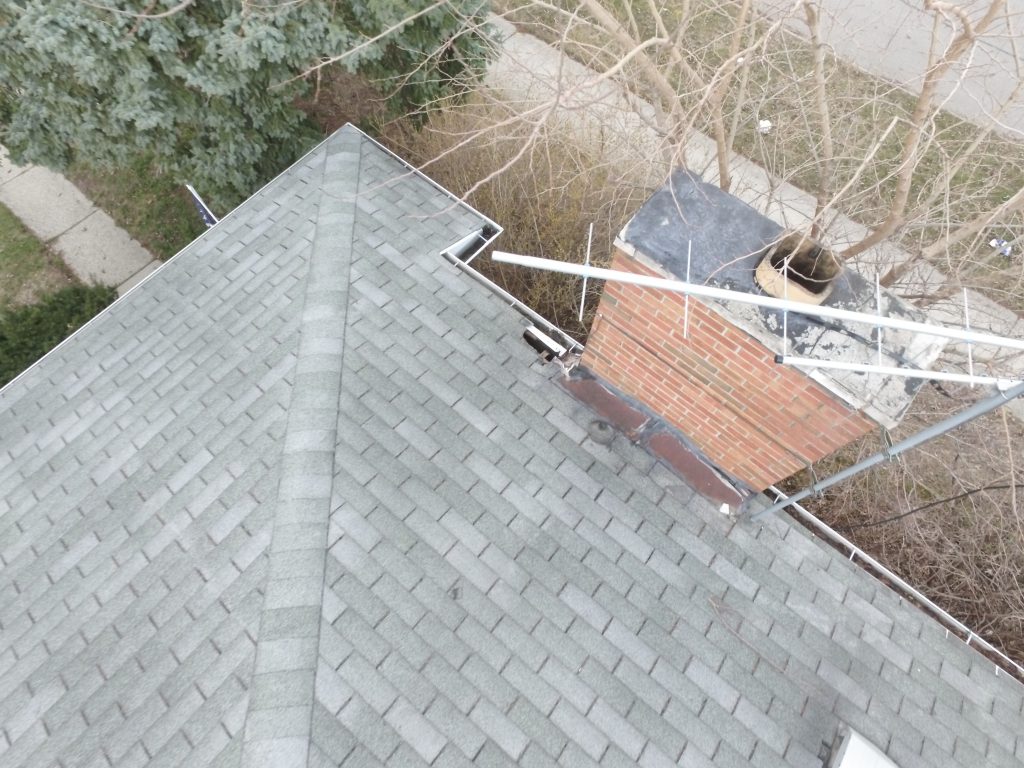 Aerial view of a residential roof and chimney, documenting visible exterior damage.